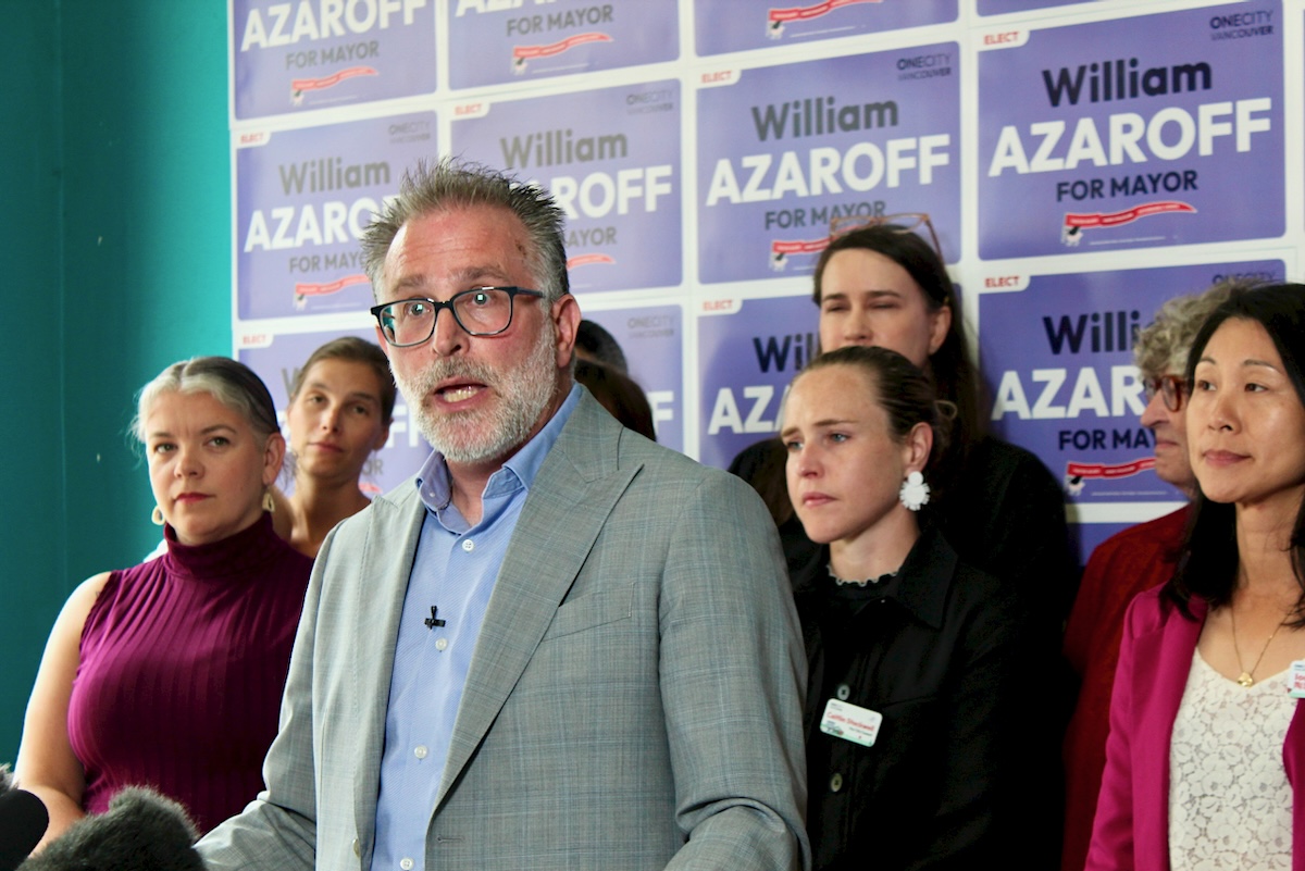A man in his 60s with short grey hair speaks in front of a lectern. 