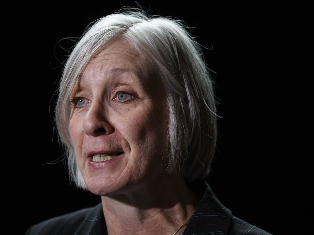 A woman in her 60s with grey hair cut in a bob style speaks against a black background.