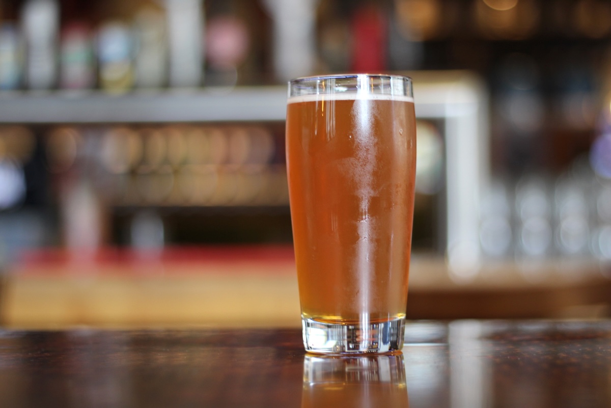 A pint of beer on a bar, with a row of taps behind it.
