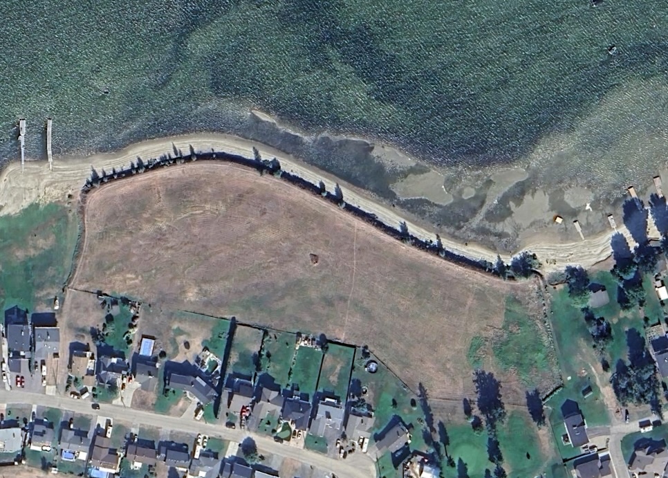 An aerial image shows a large, grassy property amid a small waterfront community.