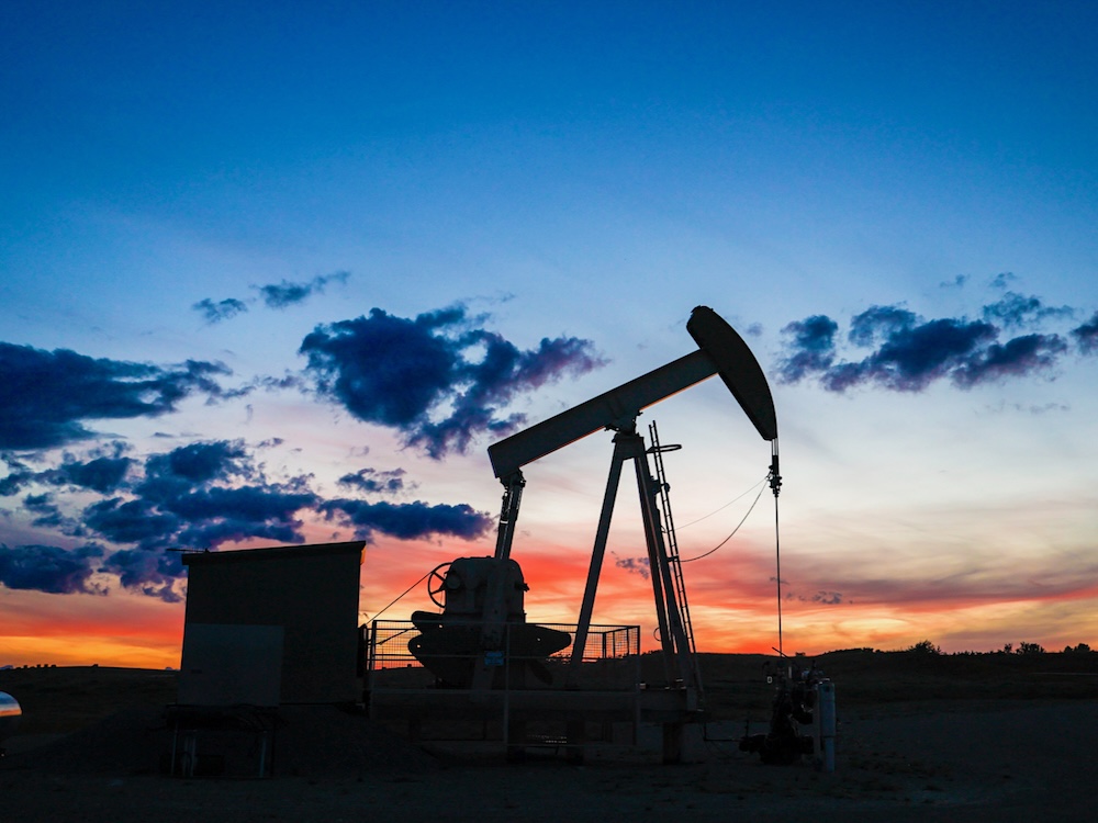 An oil pumpjack on farmland in Alberta is silhouetted against a dramatic Prairie sky at dusk.