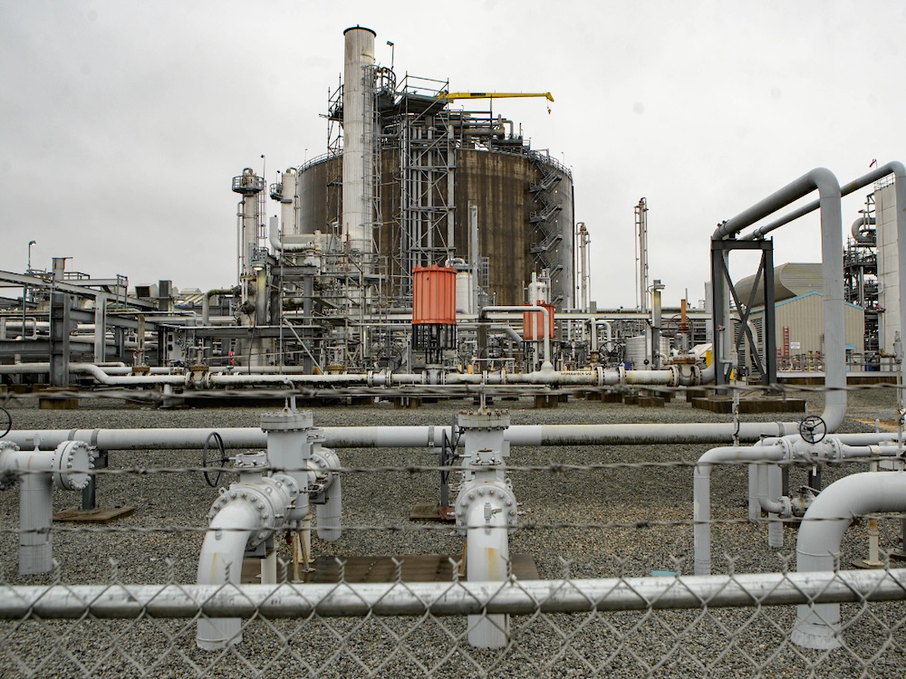 A network of pipes snakes through an energy facility. At the centre is a large cylindrical tank surrounded by pipes, and exposed metal stairs.