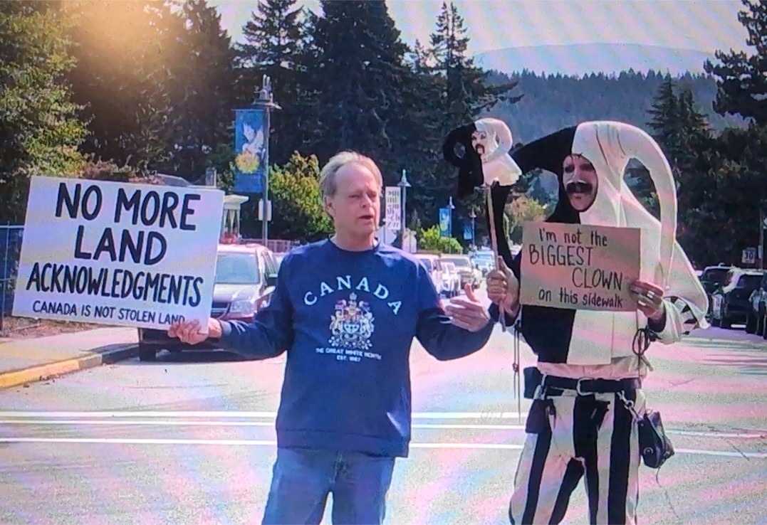 On the left, Marc Emery stands with a sign reading &lsquo;No More Land Acknowledgments. Canada is not stolen land.&rsquo; Beside him, a man in a black and white jester costume holds a sign that reads &lsquo;I'm not the biggest clown on this sidewalk.&rsquo;