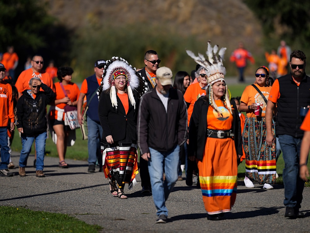Assembly of First Nations National Chief Cindy Woodhouse Nepinak, back left, and Tk̓eml&uacute;ps te Secw&eacute;pemc Chief Rosanne Casimir, front right, walk in a group of people wearing orange shirts.