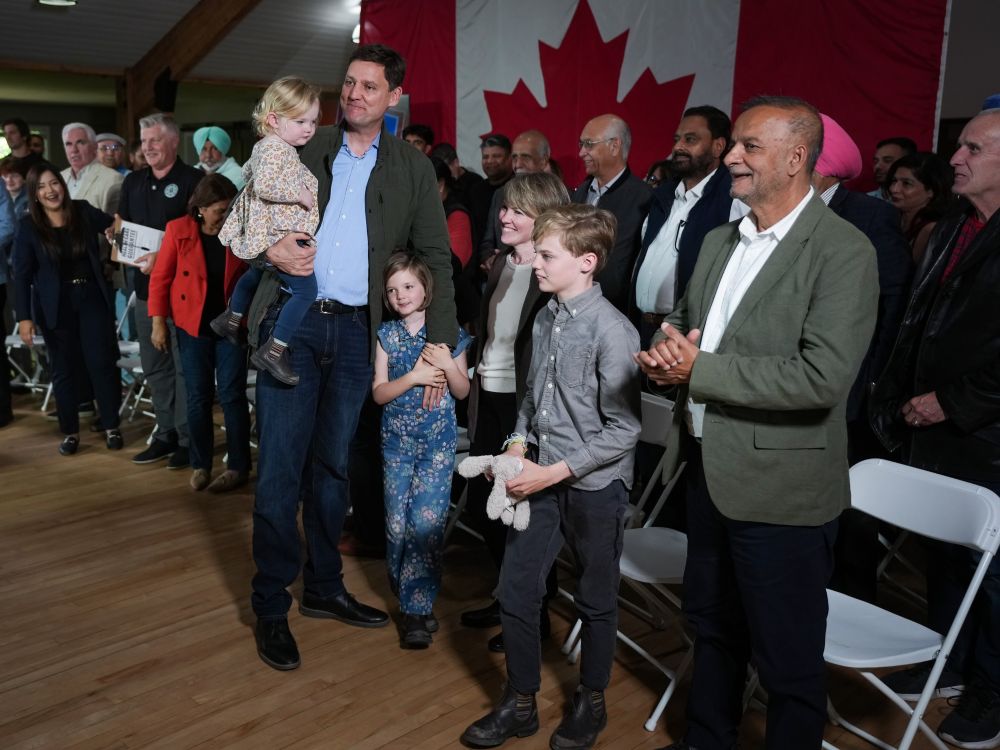 David Eby holds one child, while his spouse and two other children stand in front of a group of supporters.