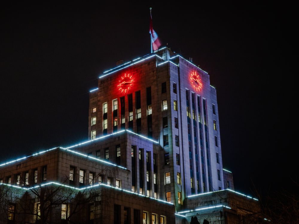 An art deco style building with a large clock at its head glows in the darkness of night time.