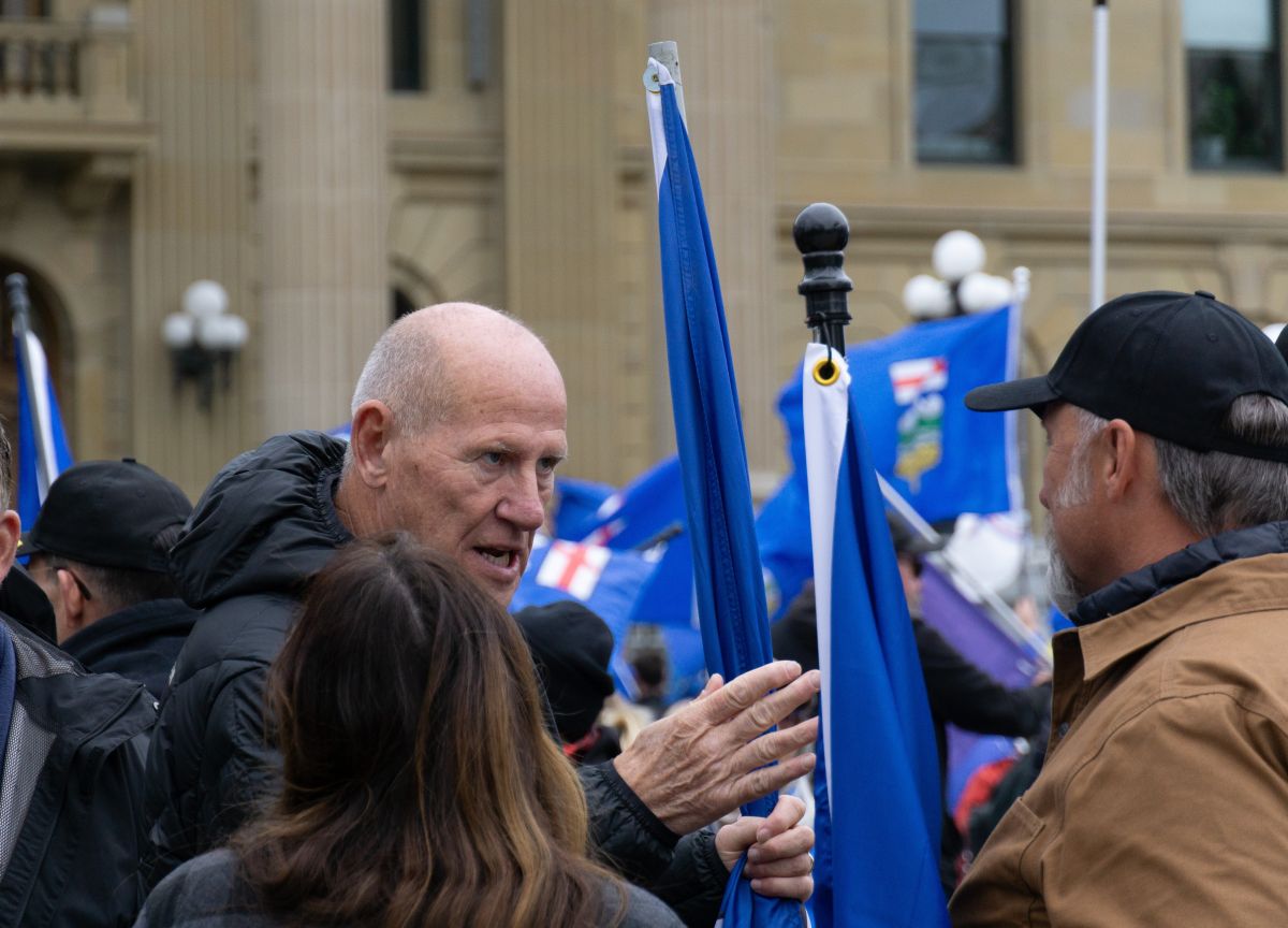 Surrounded in a crowd, a white, balding older man speaks intensely to another man.