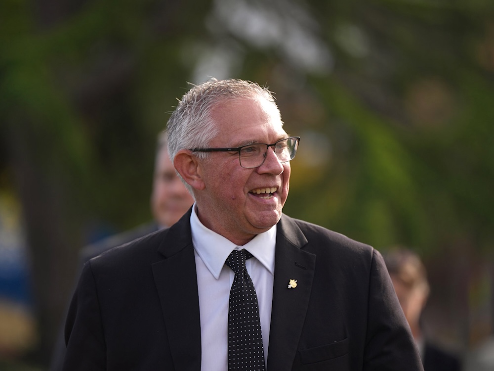 Lorne Doerkson wears a suit and glasses and smiles at someone off camera.