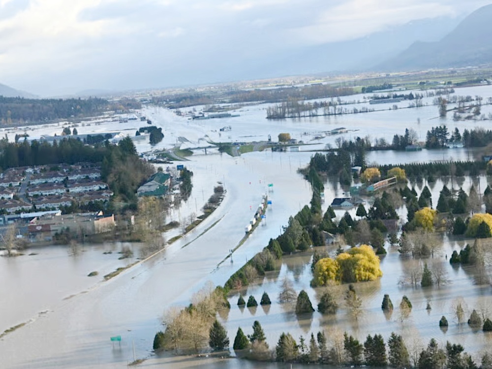 Floodwaters inundate a broad valley. The curve of a submerged highway cuts a path between a submerged golf course and a residential development on a small hill.
