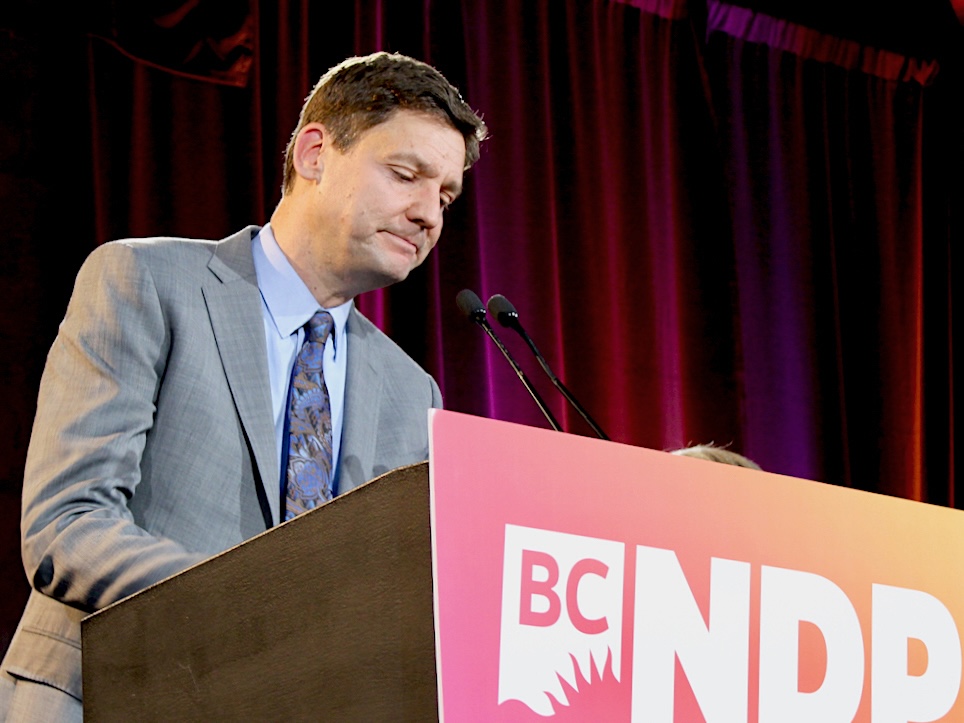 A sad-looking David Eby stands at a lectern. 
