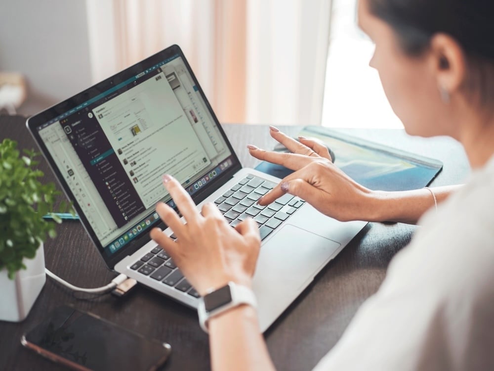 A woman in profile, blurred, typing while monitoring Slack, a workplace application that allows messaging between employees in different locations.