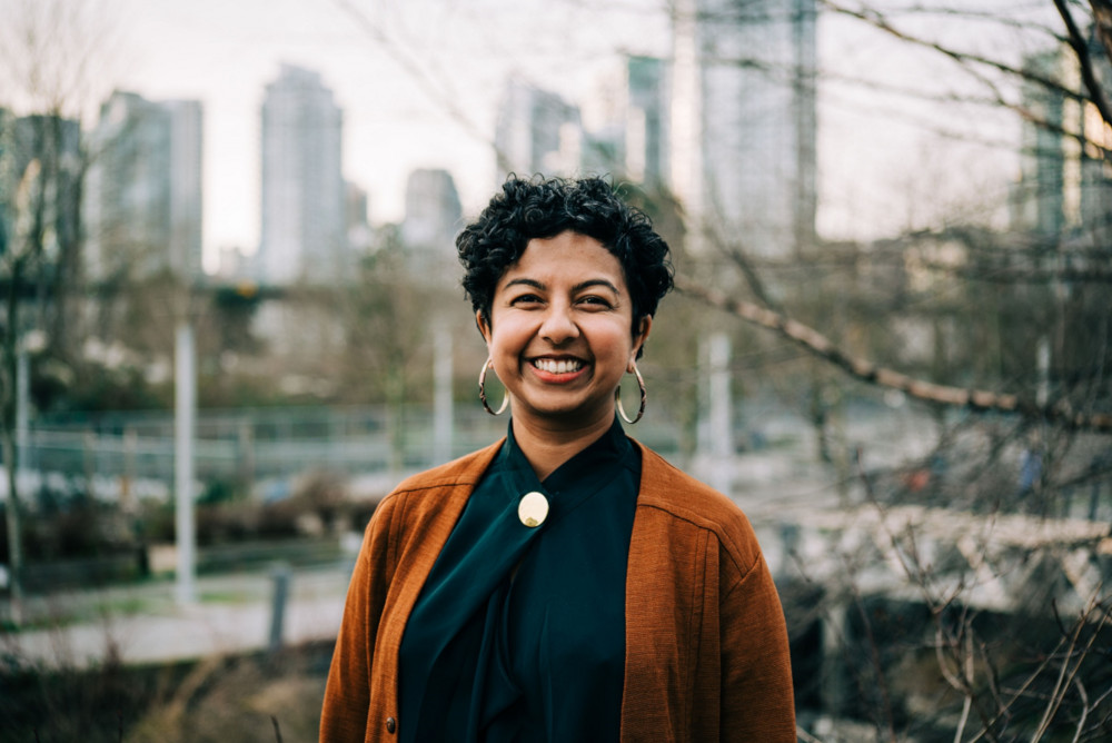 A woman smiles at the camera. She’s wearing hoop earrings and a rust-orange cardigan.