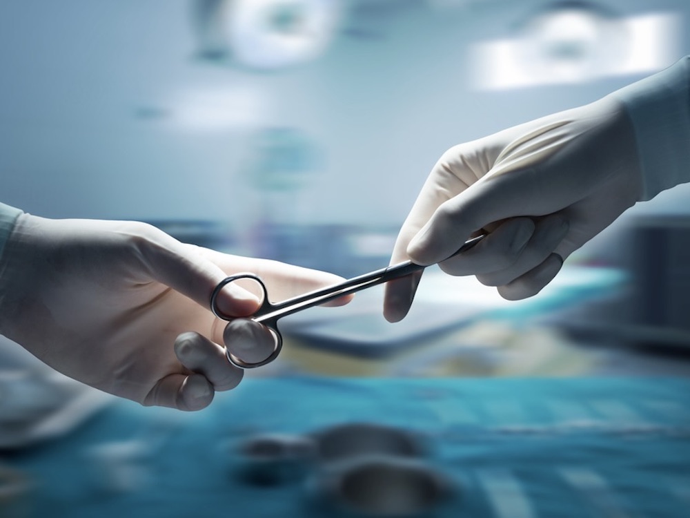 A close-up of surgical scissors being handed from one person to another in an operating room.