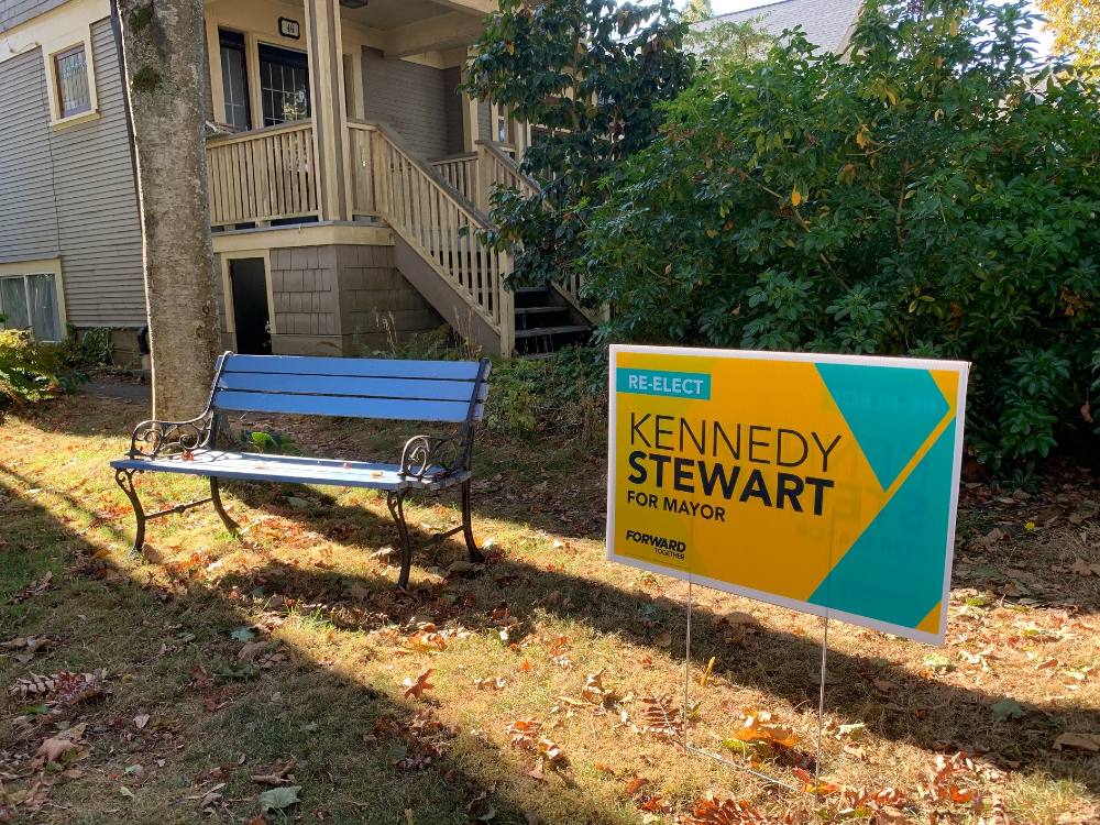 An empty bench sits aside a lawn sign for former Vancouver mayor, Kennedy Stewart