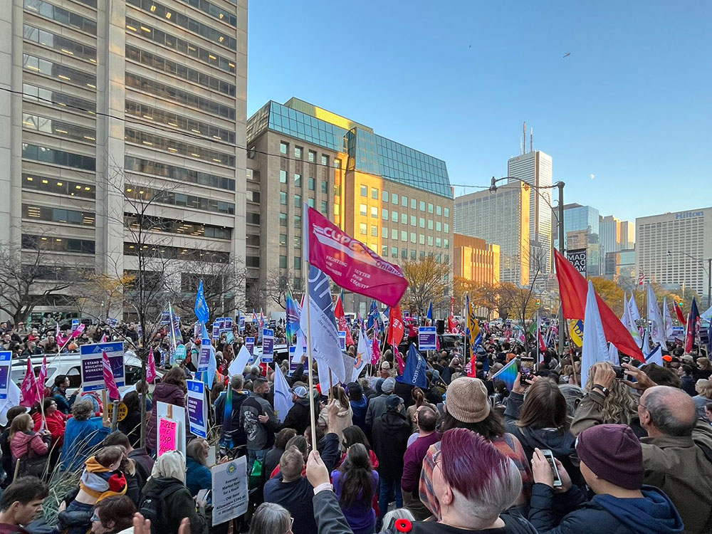A large crowd of people holding CUPE flags protest in Toronto.