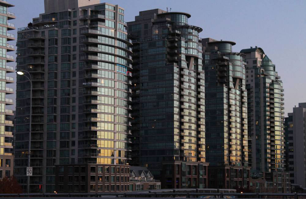 Three glassy condo towers near Science World Skytrain Station reflect the sunset to the right of the frame. 
