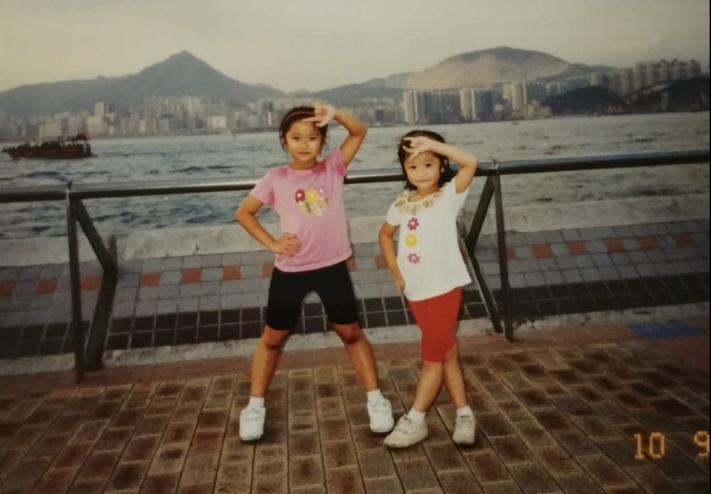 A family photo of Jenn Chan, left, and Nicole Chan as children. They are posing at a waterfront location and wearing summer clothes.