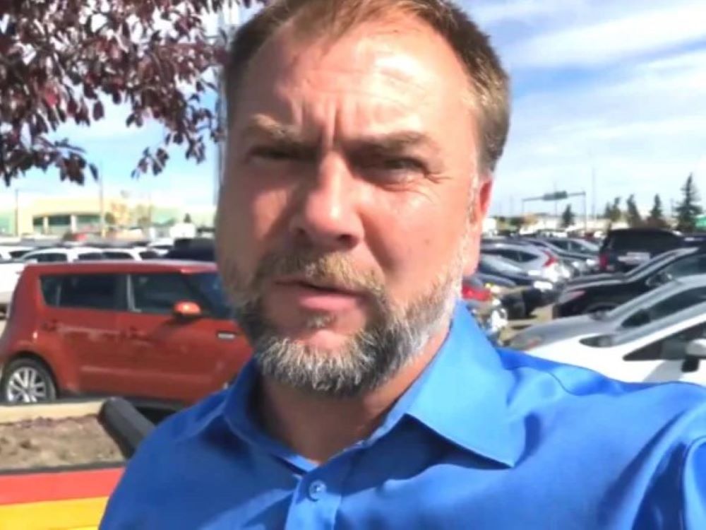 Artur Pawlowski, in a blue shirt, looks at the camera in a parking lot.