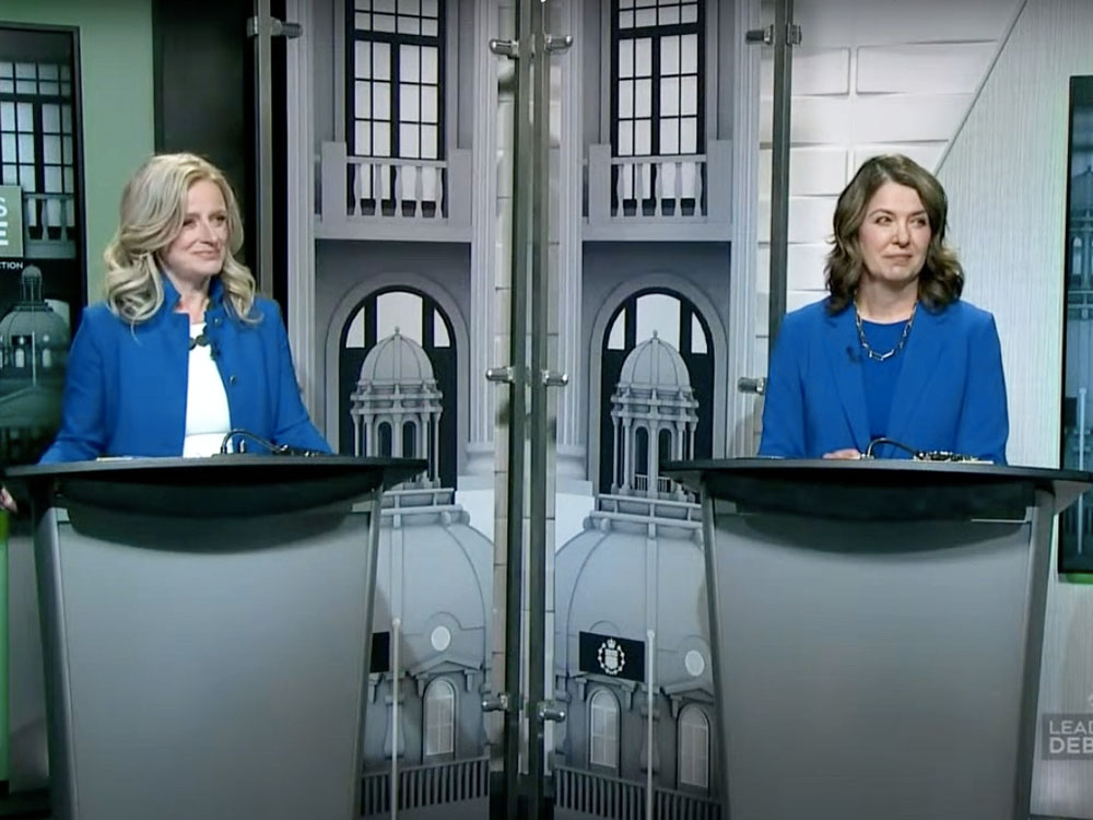 Rachel Notley and Danielle Smith are on a stage for the televised leaders’ debate. Both wear light blue suits.