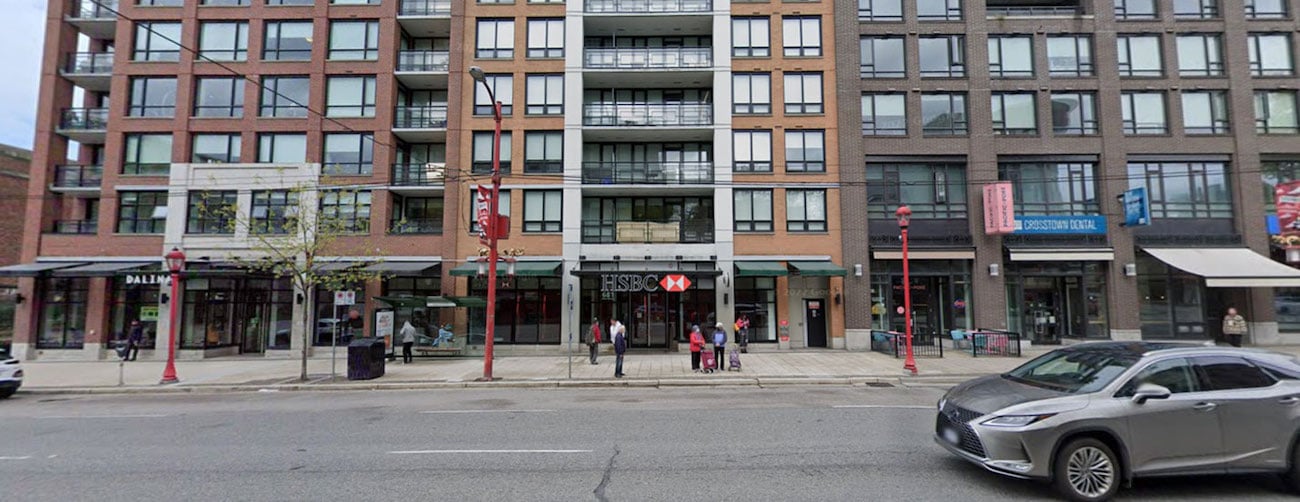 A horizontal photo from Google Street View in 2023 depicts a wide brown condo building with an HSBC bank on the main floor.