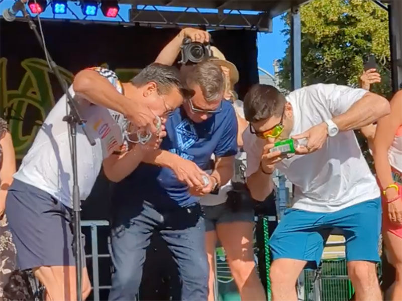 Three men on a stage are gulping beer from cans.