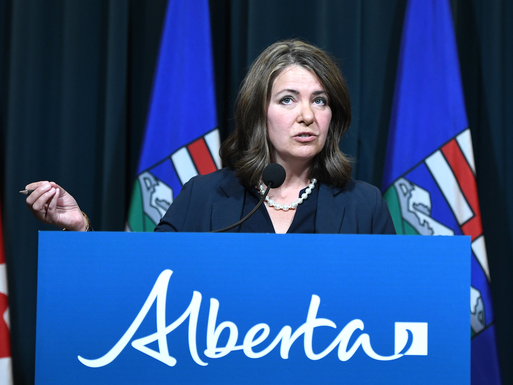 Danielle Smith stands behind a podium with Alberta flags in the background.