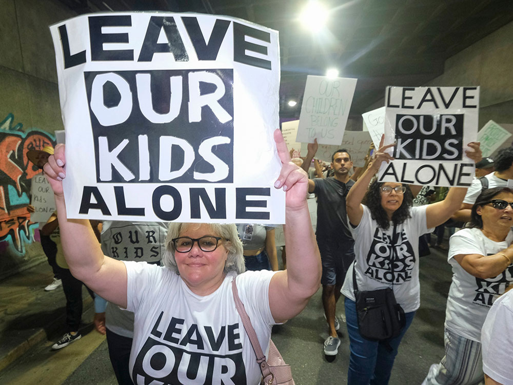 Protesters march carrying signs that say “Leave Our Kids Alone.”
