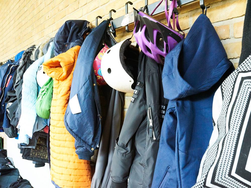 Children’s jackets and bike helmets are hung up on a coatrack at school.