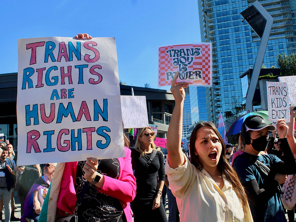 Counter-protesters at a rally opposing sexual orientation and gender identity education in schools hold colourful signs saying ‘Trans Rights Are Human Rights’ and ‘Trans Joy Is Power’ on a sunny day in Vancouver.