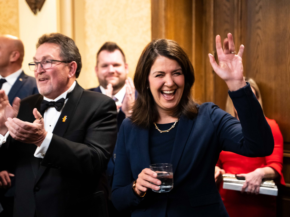 Danielle Smith attends a party in a dark blue blazer. She smiles and finger-waves at someone off-camera.