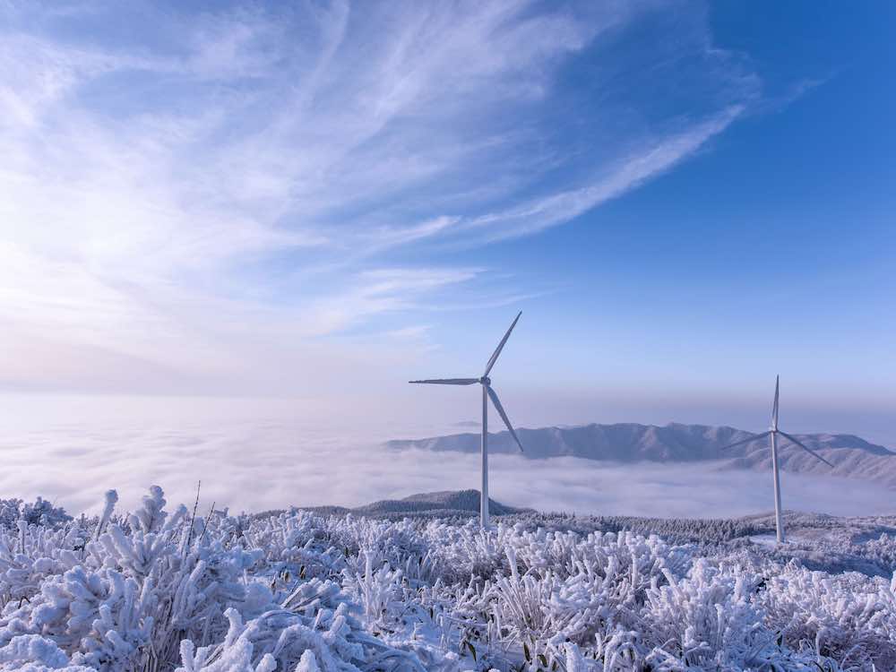 A wind turbine stands under a blue sky, with a mountain in the background and ice formations in the foreground.