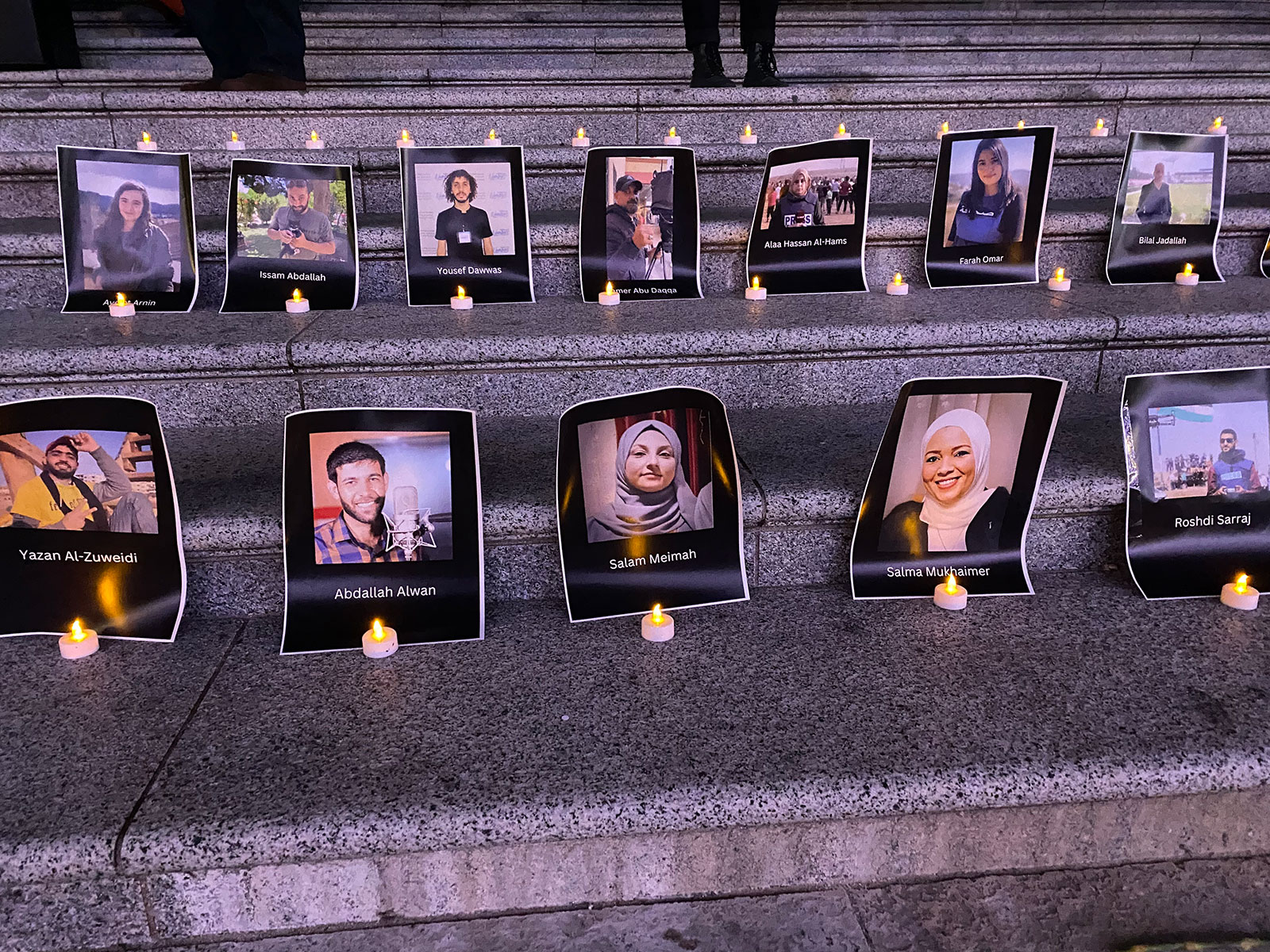 Photographs line rows of concrete steps. In front of each photo is a small plastic tea light candle. The photos are headshots of journalists killed in Gaza, Israel and Lebanon during the Israel-Hamas war.
