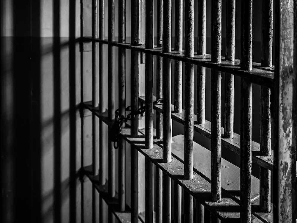 A black and white photo shows grey prison bars.