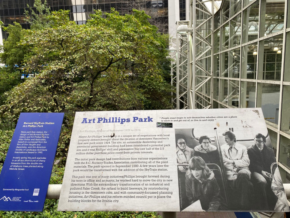 A plaque titled “Art Phillips Park” with text and a photo in front of a small tree.