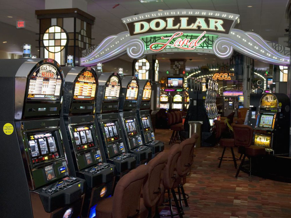 A row of slot machines and chairs stand on a rust-coloured with an overhead sign that says “Dollar Land.”