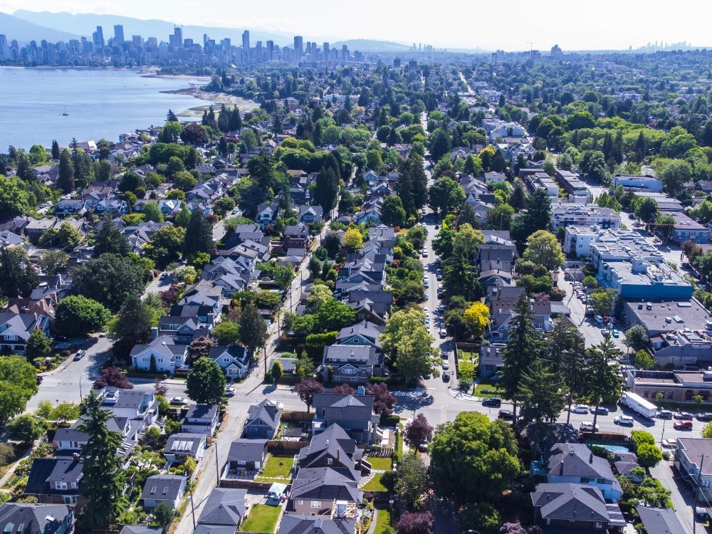 An aerial view of a leafy, largely low-rise neighbourhood with the edge of a bay and a city skyline in the distance.