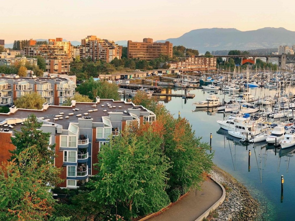 An aerial view of False Creek South, as the Vancouver seawall rounds a bend with townhouses to the right and small boats anchored in the harbour to the right.