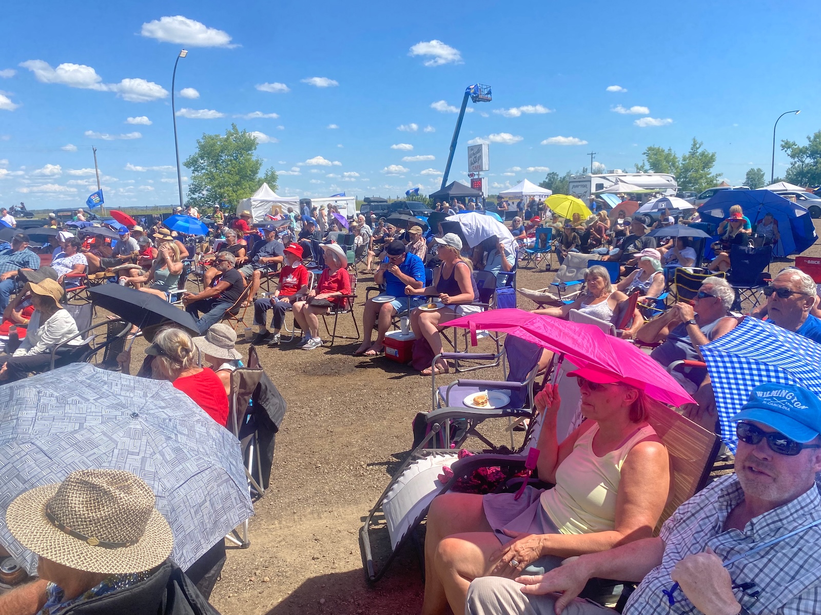 People sit in lawn chairs, many holding umbrellas as shields from the sun.