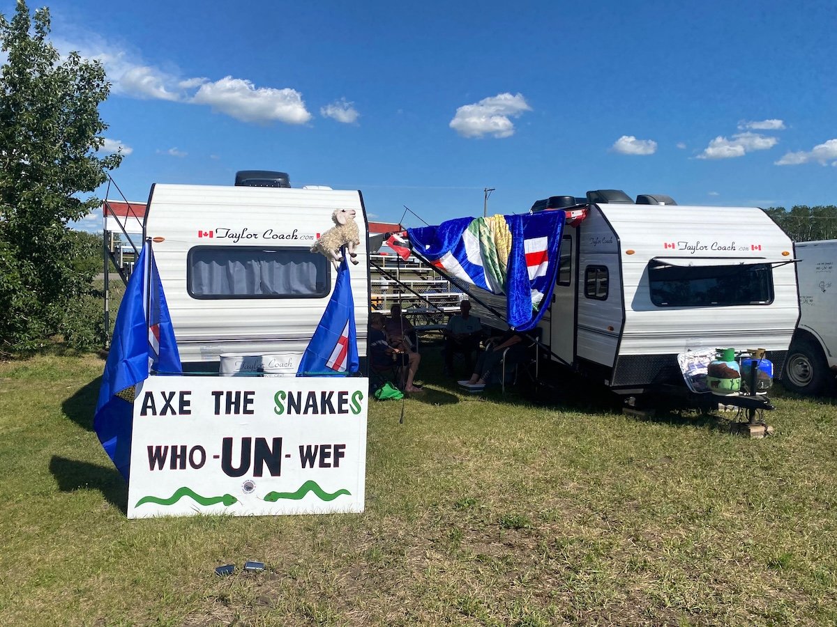 Two travel trailers are festooned with Alberta flags. One has a sign that says ‘Axe the snakes: WHO, UN, WEF.’