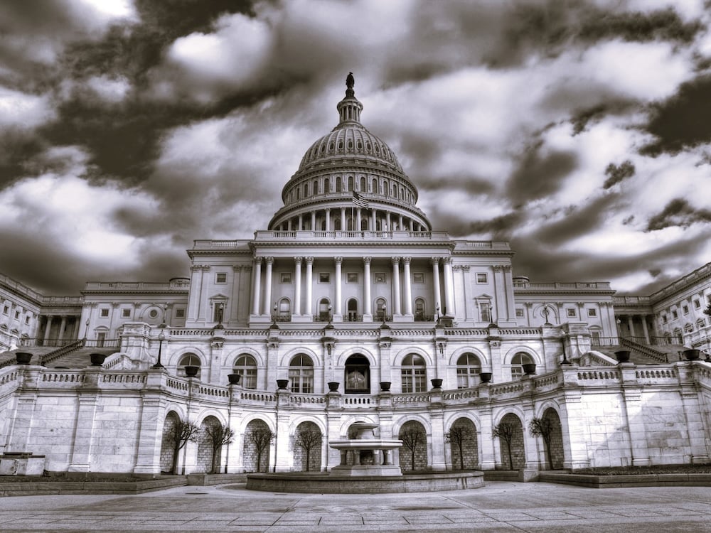 A stylized black and white image of the U.S. Capitol building beneath cloud-dotted skies.