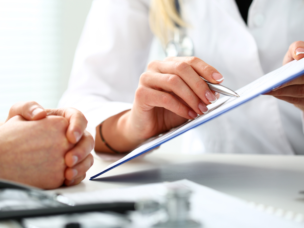 A person wearing a white coat and stethoscope shows a consent form to a patient.