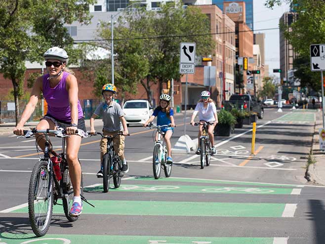 A single file of four cyclists wearing helmets, including two children, on city bike lanes in the warm weather. 