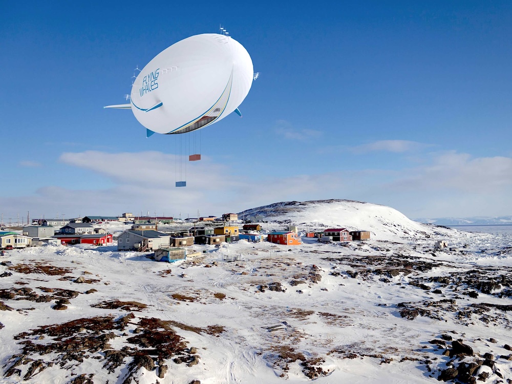 A digital rendering depicts a large white airship depositing or picking up shipping containers of supplies in a small northern community in a snowy climate against a blue sky.