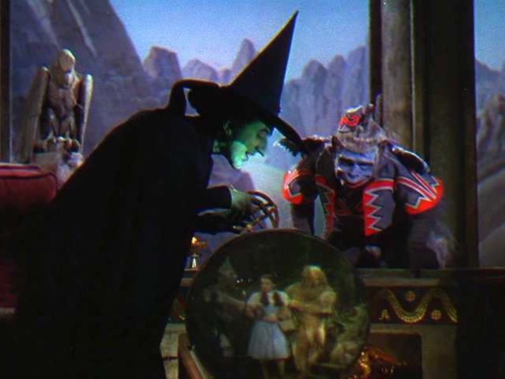 The Wicked Witch of the West peers into a crystal ball with a flying monkey.