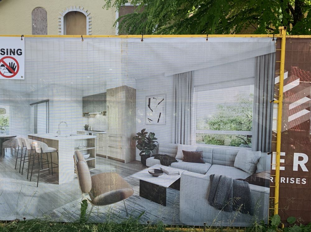 An ad on a fence outside a construction site shows the interior of a new apartment.