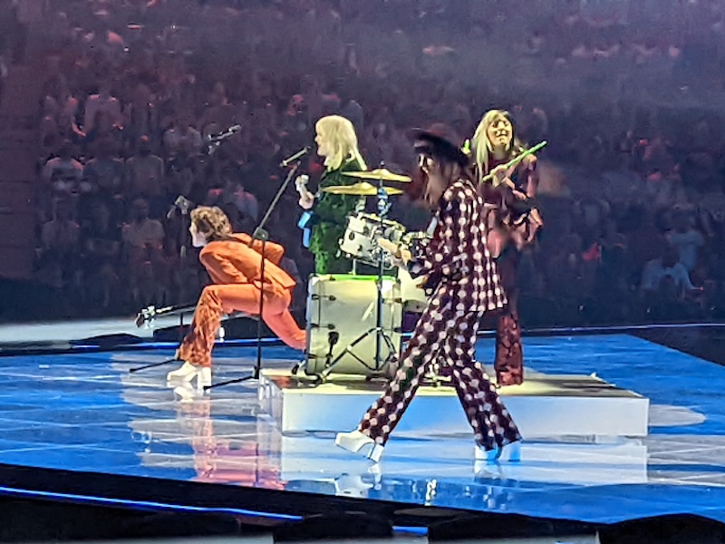 Four musicians in striking costumes perform on a grand stage.