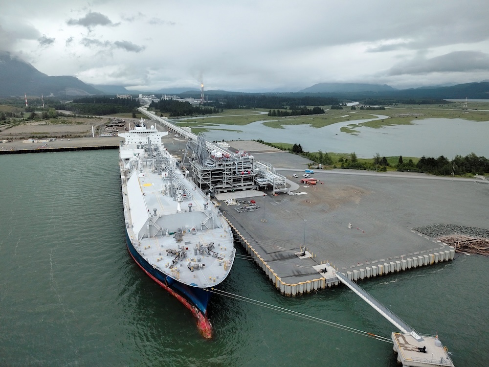 A large ship with raised tanks on its deck is tied to a dock on a cloudy day.