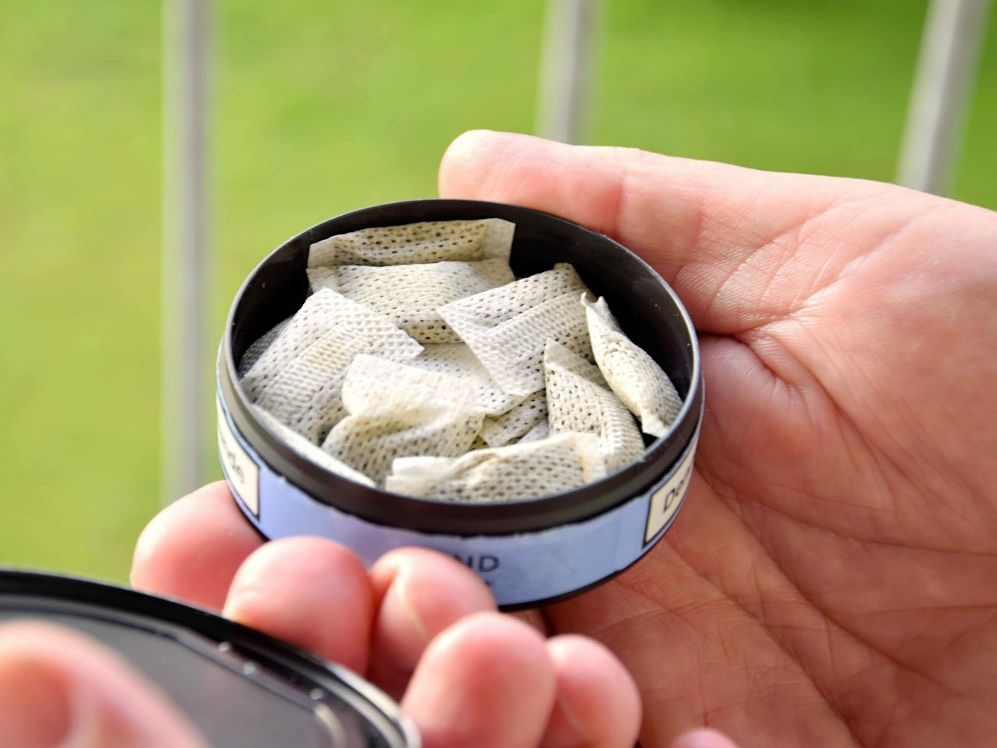 A hand is holding a small round container with nicotine pouches.