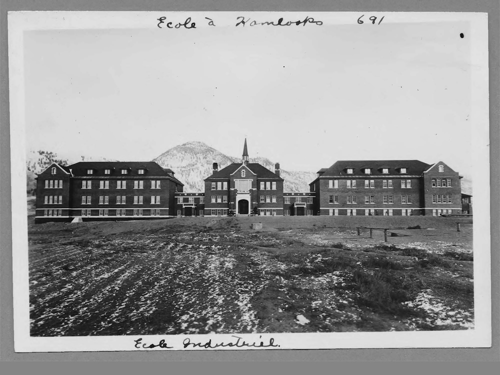 A black and white photo shows the Kamloops Indian Residential School. 
