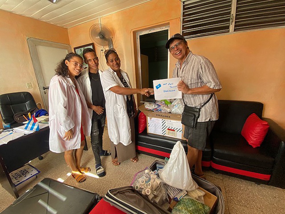 Three doctors in white coats, left, accept a donation of medical supplies from a Canadian man. He is holding a &ldquo;Not Just Tourists Vancouver&rdquo; sign and reaching over to shake a doctor&rsquo;s hand.